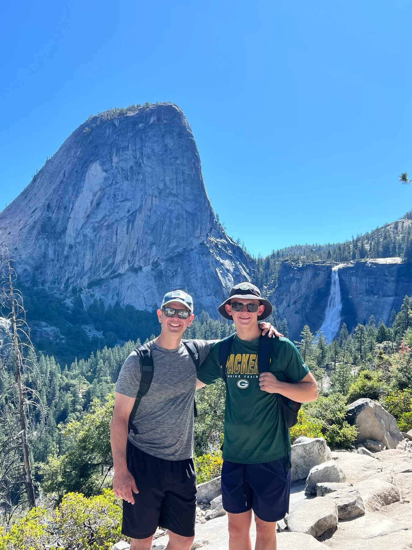 Two hikers in Yosemite in front of a granite cliff and waterfall